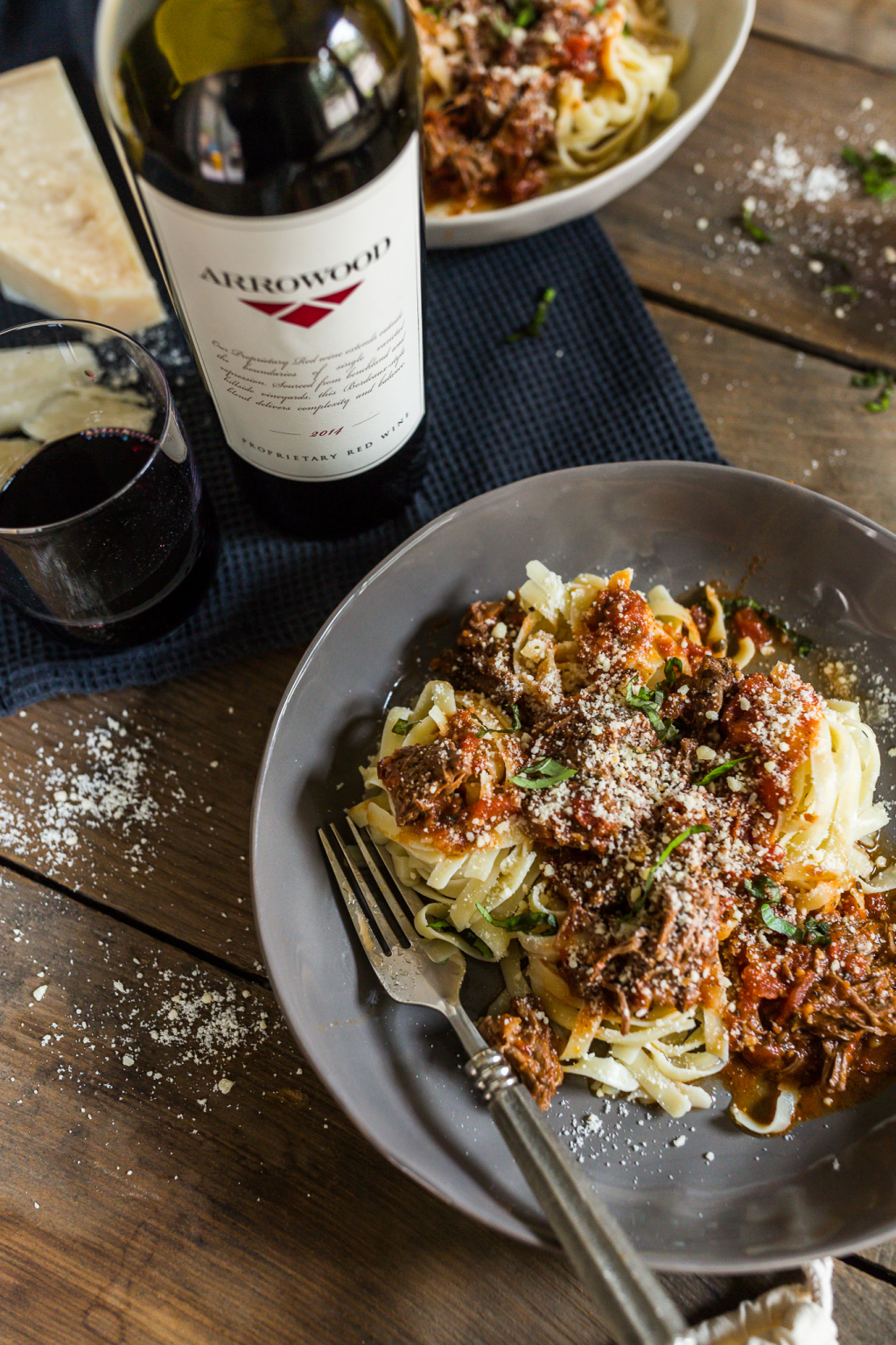 A plate of red wine braised short rub ragu over tagliatelle pasta with a bottle of Arrowood wine next to the plate on a table.