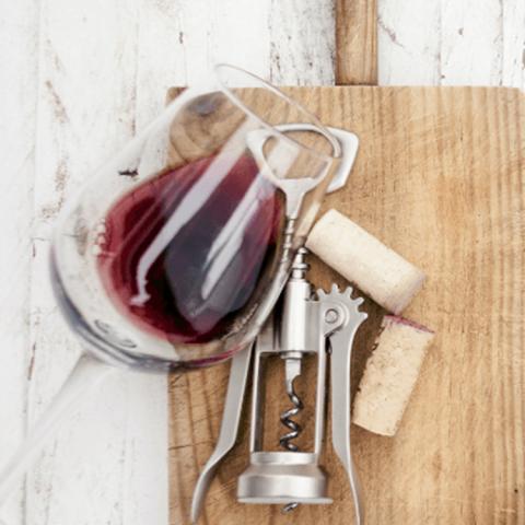 A glass of Arrowood Vineyards red wine laying on a wooden board with a cork screw and a couple corks.