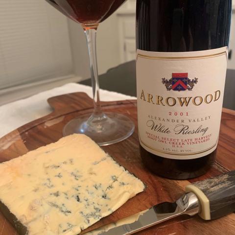A bottle of Arrowood vineyard's late harvest riesling on a wooden tray next to a triangle of blue cheese.