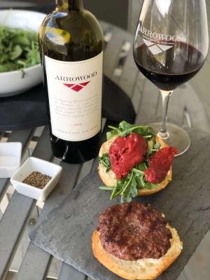 A wine bottle of Arrowood Vineyards Proprietary Red paired with a lamb burger plated on a slate dish.