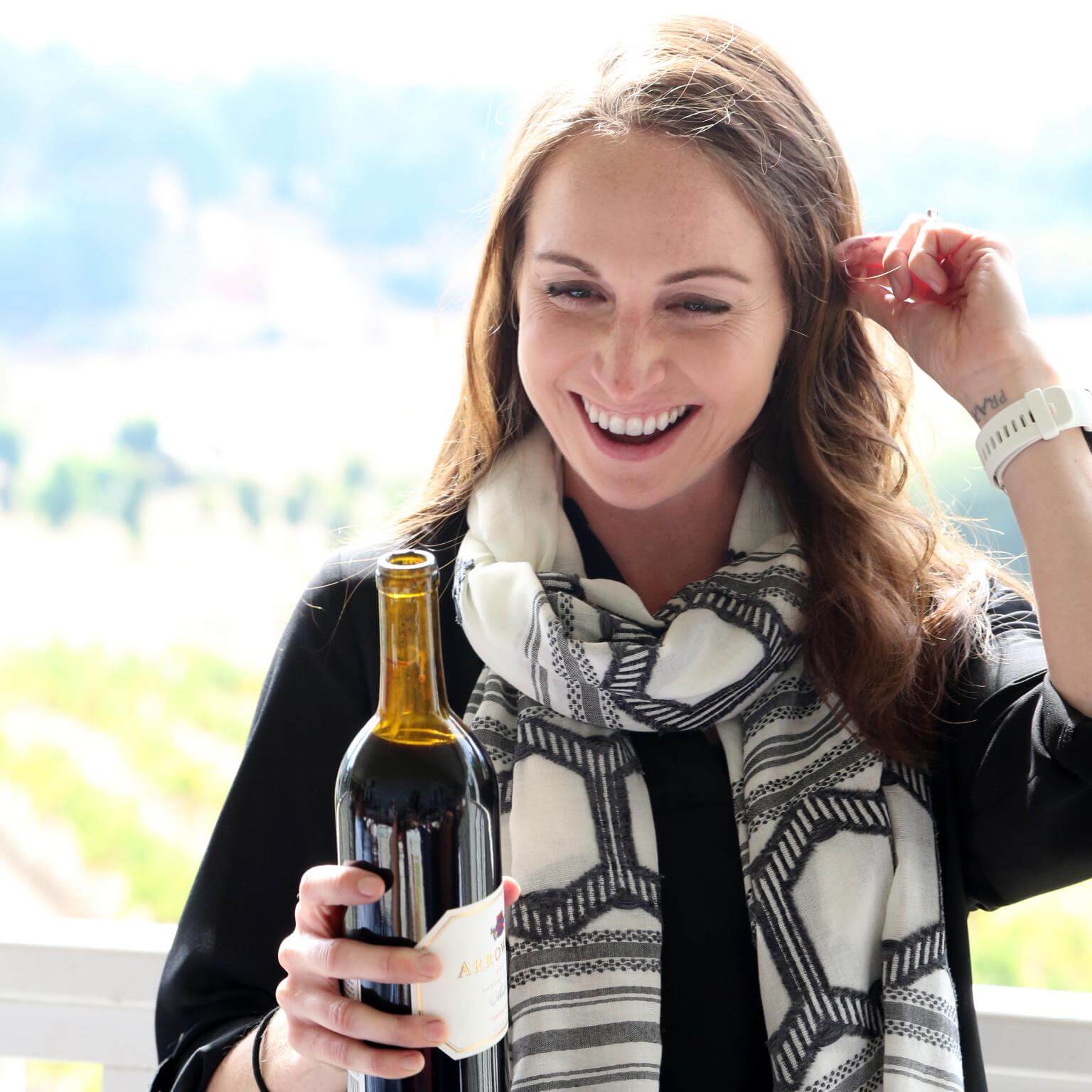 Arrowood Winemaker, Kristina Shideler, holding a bottle of Arrowood Vineyard's wine and smiling.