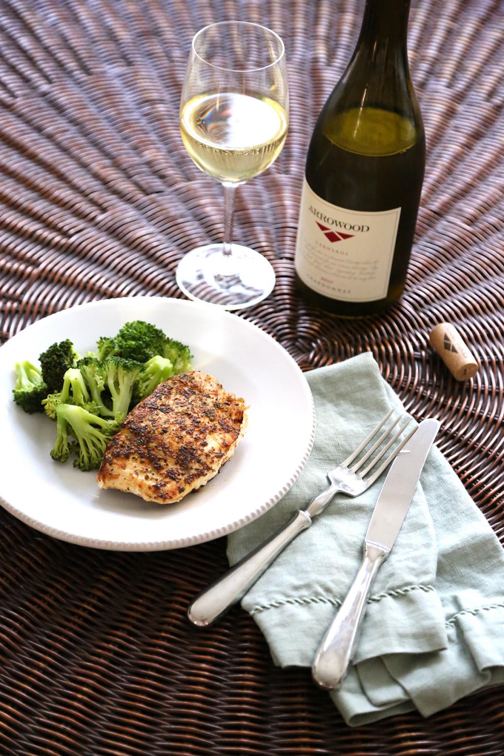 A bottle of Arrowood Chardonnay on a table with plated meal of fish and broccolli. 